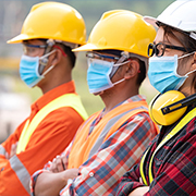 Close sideview of three construction workers in hard hats and masks with arms crossed