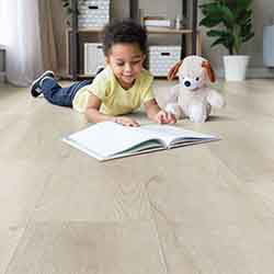 Child laying on floor reading book to teddy bear